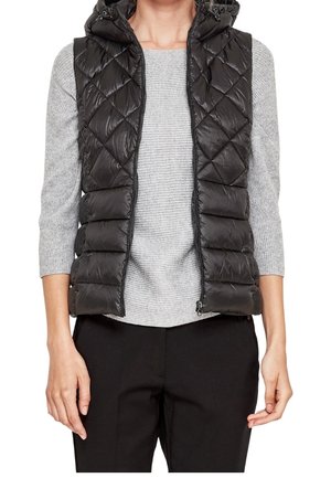 Woman wearing a black quilted sleeveless puffer vest over a light gray ribbed three-quarter sleeve top and black pants.
