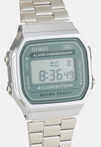 Montre en acier inoxydable argenté avec écran digital vert, fonction d'alarme chronomètre, étanchéité et design de boîtier rectangulaire.