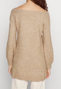 Maglione color beige, off-the-shoulder, con maniche lunghe a palloncino. Texture morbida e dettaglio a coste sull'orlo, che raggiunge la lunghezza a metà coscia.