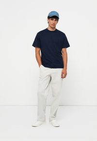 Marine blauw T-shirt met korte mouwen, relaxed fit, gecombineerd met lichtgrijze wijde broek en witte sneakers. Een blauwe pet maakt de outfit compleet.