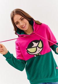 Mikina s jasně růžovou horní částí a zelenou spodní částí, se velkým kresleným charakterem umístěným uprostřed přední strany.