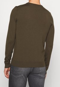 Olivgrüner Strickpullover mit Rundhalsausschnitt und langen Ärmeln. Glatte Textur mit gerippten Bündchen und Saum, kombiniert mit dunkelgrauen Jeans.