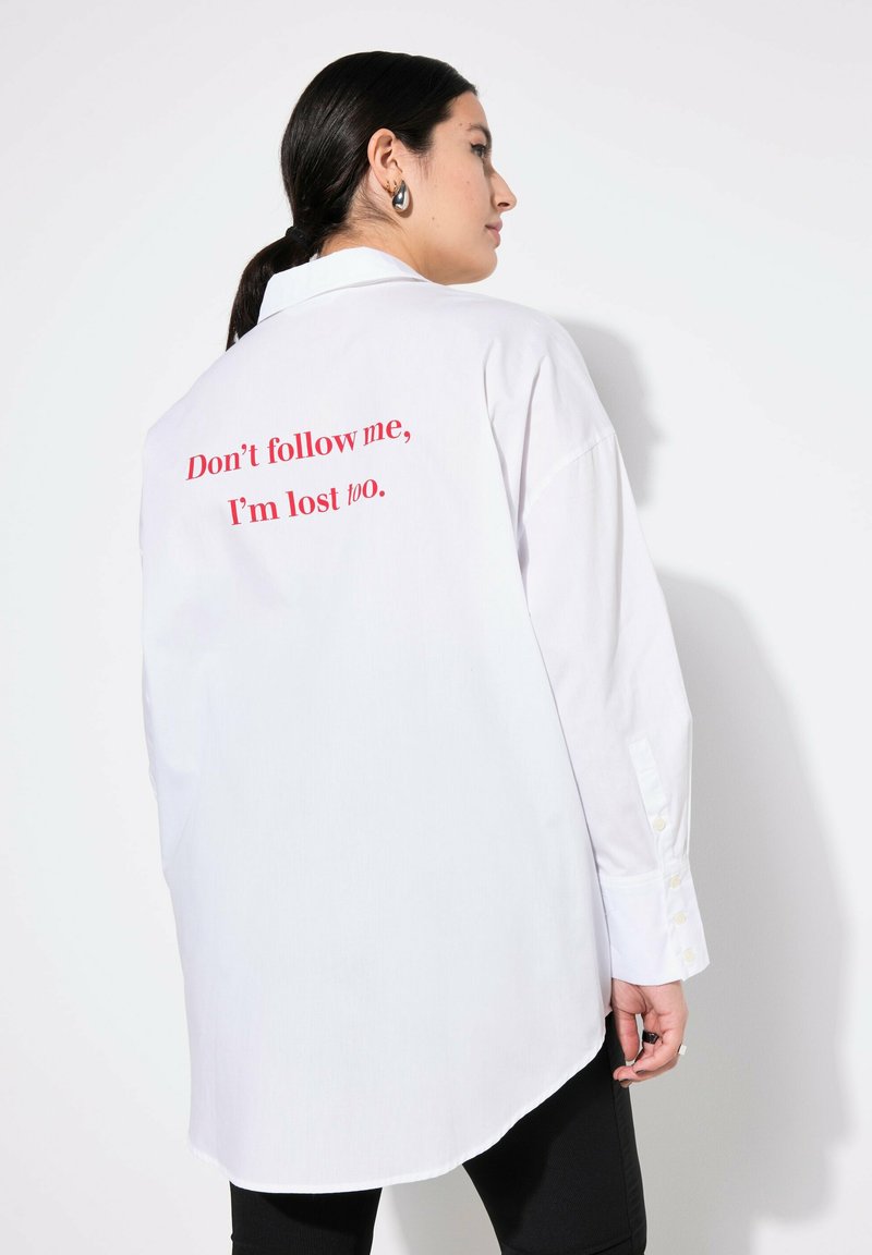 Camicia bianca over-size con orlo dritto, maniche lunghe e testo rosso sul retro che recita: "Non seguirmi, anche io sono perso."