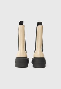 Bottes ankle élégantes avec un devant beige et des côtés noirs, dotées d'une semelle épaisse et de tirants à l'arrière, présentées de derrière.