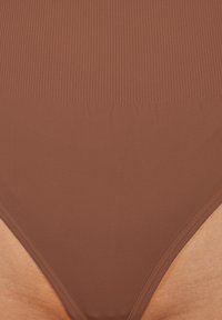 Parte inferiore di costume da bagno marrone con design senza cuciture. Caratterizzata da una superficie liscia e una copertura media con apertura alta sulle gambe.
