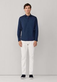 Granatowa koszula z długim rękawem, noszona z białymi spodniami i czarnymi butami. Koszula ma gładką fakturę i dopasowany krój.