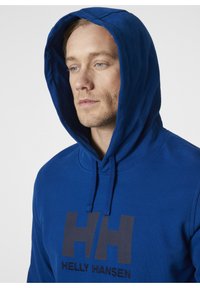 Sudadera azul hecha de una tela suave, con un gran logo "HH" en gris oscuro en el frente y capucha ajustable con cordones.