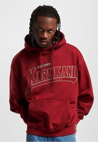 Burgunder hettegenser med lommeslipp foran og brodert "KARL KANI EST. 1989" logo i hvitt og grått, med ribbestrikkede cuffs og kant.