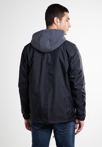 Czarna lekka kurtka z szarym kapturem, o gładkiej fakturze, z elastycznymi mankietami i nieco luźnym krojem, zaprojektowana z myślą o codziennym noszeniu.