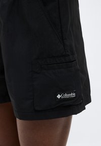 Μαύρα cargo σορτς Columbia Sportswear με πλαϊνή τσέπη στο μηρό ενός ατόμου, πάνω σε απλό ανοιχτό φόντο.