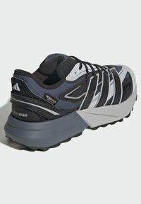 Schwarzer, grauer und weißer Sneaker aus Mesh- und Synthetikmaterialien. Verfügt über eine strukturierte Gummisohle, mehrere Paneele und Markenlogos.