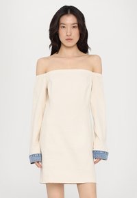 Rochie crem cu umeri lăsați, cu mâneci lungi, având manșete din denim albastru, un bust înfășurat și o siluetă dreaptă.