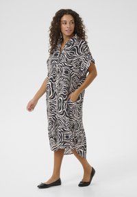 Abito midi a fantasia zebra con colletto, maniche corte, tasche laterali e vestibilità comoda, disponibile nei colori nero e crema.