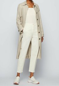 Beige trenchcoat med stora knappar, vit åtsittande topp och krämfärgade byxor. Skorna är vita sneakers med rosa detaljer.