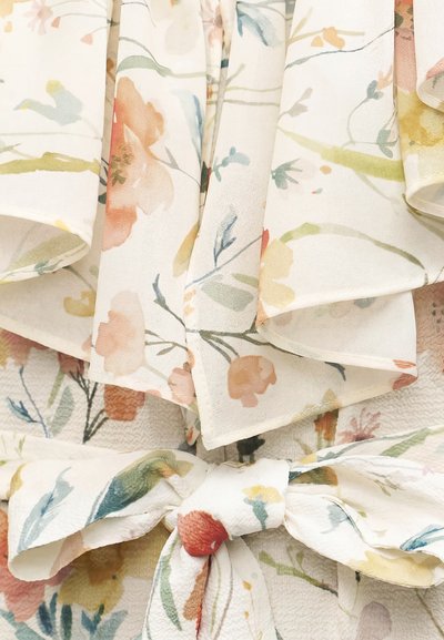 Υφασμα ανοιχτού χρώματος με απαλό λουλουδάτο σχέδιο σε παστέλ αποχρώσεις, με στρωματώδη πτυχώσεις και δεμένο φιόγκο στο κέντρο.