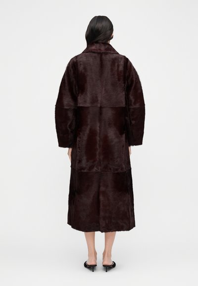 Rudos dirbtinio kailio paltas su tiesia siluetu, dideliu apykakle ir ilgomis rankovėmis. Dizainas siekia kelius, pasižymi lygiu tekstūros paviršiumi.