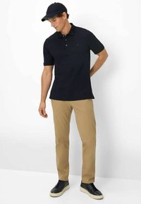 Navy polo shirt, short sleeves, three-button placket. Beige chinos, straight leg, paired with black sneakers. Cap complements the outfit.