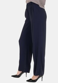 Pantaloni a gamba larga color navy con una texture liscia, caratterizzati da pieghe anteriori e chiusura con zip. Abbinati a tacchi alti neri per creare contrasto.
