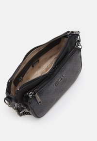 Musta teksturoitu käsilaukku, jossa on vetoketjullinen osasto, beige vuori ja brändin nimi "Guess" kohokuvioituna edessä. Mukana toimitetaan ketjusta valmistettu olkahihna.