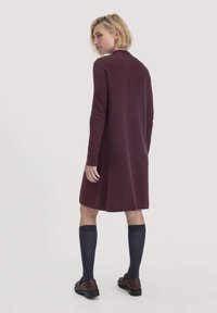 Bordeauxfarbenes Strickkleid mit langen Ärmeln, endet oberhalb des Knies. Kombiniert mit knielangen marineblauen Socken und braunen Schuhen, glatte Textur, minimalistisches Design.