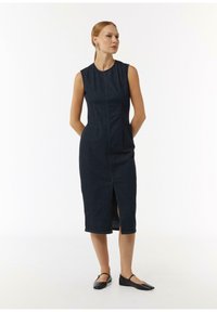 Sukienka jeansowa, ciemnoniebieska, bez rękawów, prosty krój z przednim rozcięciem, teksturowana tkanina, długość do kolan, zestawiona z czarnymi balerinami.