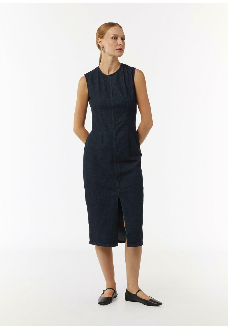 Sukienka jeansowa, ciemnoniebieska, bez rękawów, prosty krój z przednim rozcięciem, teksturowana tkanina, długość do kolan, zestawiona z czarnymi balerinami.