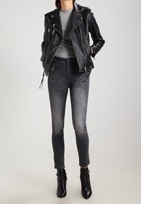Černá kožená motorkářská bunda přes šedé tričko s dlouhým rukávem, v kombinaci se šedými skinny džínami a černými kotníkovými botami. Hladké textury, přiléhavý střih.