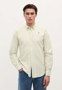 Camicetta a righe in tessuto giallo chiaro con colletto botton-down e un piccolo logo ricamato; abbinata a jeans in denim blu.