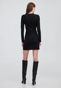 Zwarte lange mouwen mini-jurk met een aansluitend ontwerp en ronde halslijn, gecombineerd met knie-hoge zwarte leren laarzen met hak. Gladde textuur.