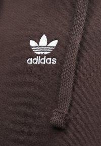 Καφέ φούτερ με κουκούλα, με υφή υφάσματος, λευκό κεντητό λογότυπο Adidas trefoil και λεπτομέρεια κορδονιού στην κουκούλα.