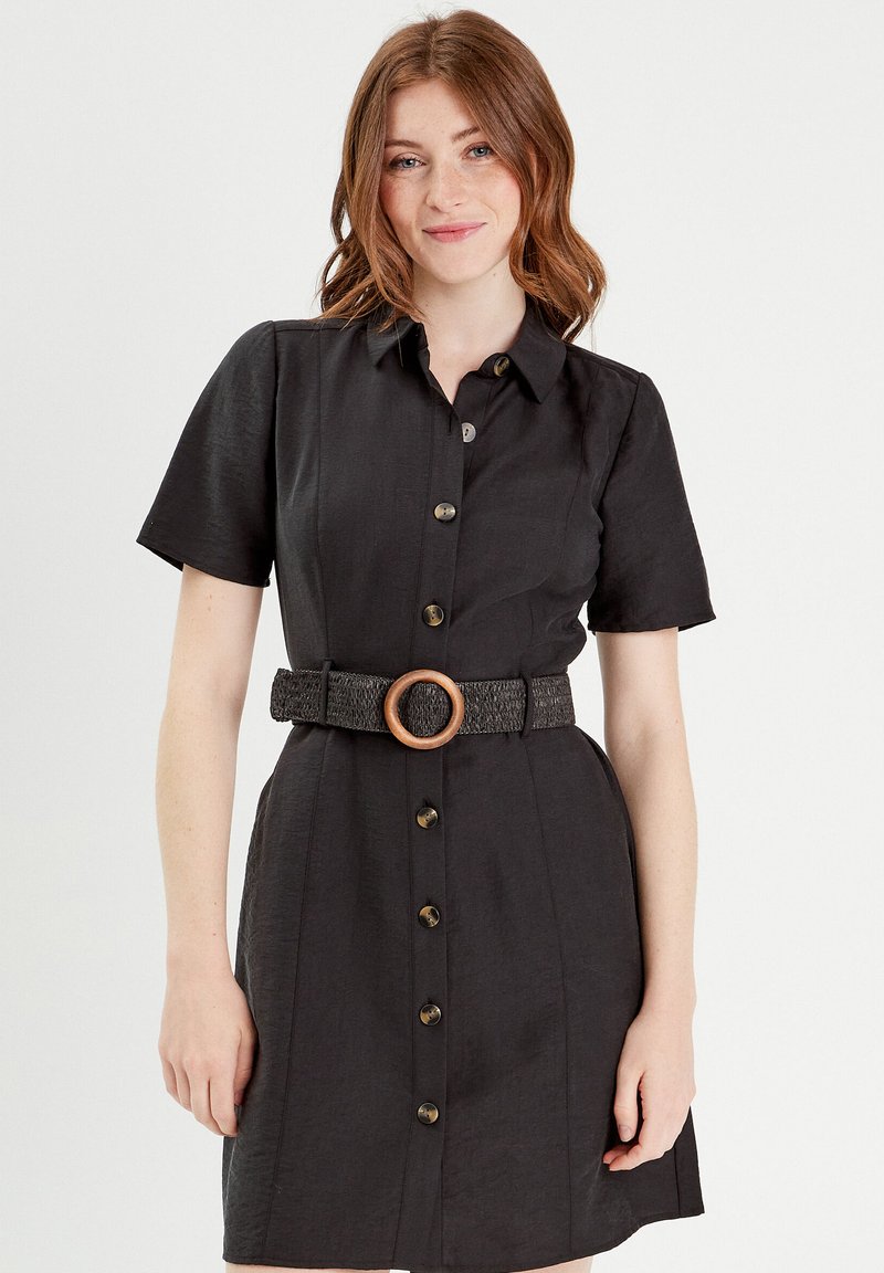 Robe noire à manches courtes, col et boutons sur le devant. Dotée d'une ceinture à la taille texturée avec un détail en anneau en bois. Tissu lisse.