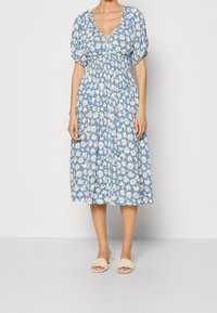 Blauwe bloemenjurk met puffmouwen en een V-hals. Heeft een tailleriem en een rok tot op de knie, versierd met witte madeliefjespatronen.