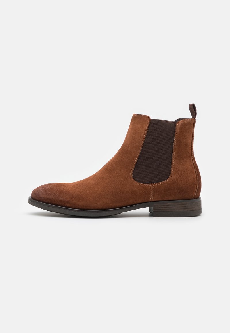 Bottine Chelsea en daim marron avec panneau latéral élastique noir et petit talon empilé sur fond blanc.