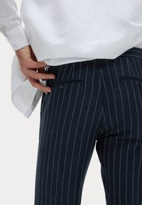 Pantalons à rayures marines en tissu texturé, avec une taille lisse, des poches avant et de petits boutons décoratifs.