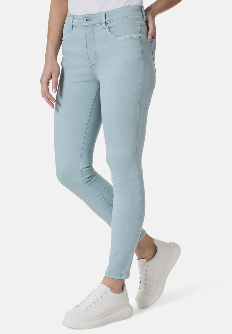 Helle blaue enganliegende Jeans aus Denim mit mittelhohem Bund, dezenten Stichdetails und Fronttaschen, kombiniert mit weißen Sneakers.