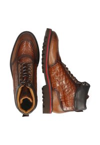 Botas de cuero marrón con textura grabada de cocodrilo, acentos marrones suaves, punta redondeada y suela de goma negra resistente. Ribete rojo en la suela.
