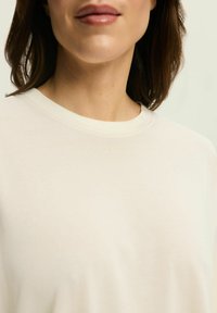 Cream-colored, short-sleeved t-shirt with a round neckline and a subtle textured finish. Embroidered logo in light color on the chest.