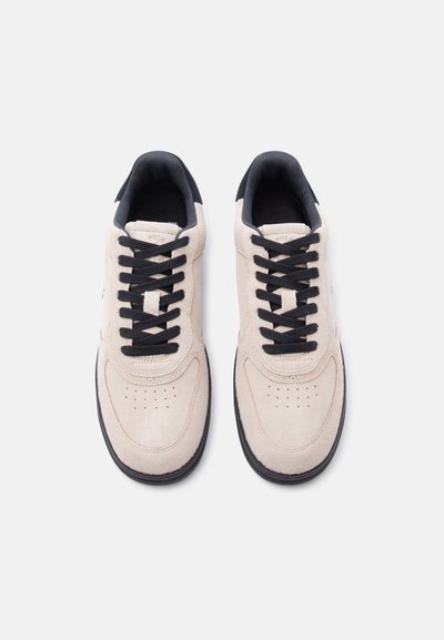 Ζευγάρι μπεζ σουέντ αθλητικά παπούτσια με μαύρα κορδόνια και μαύρες σόλες, σε θέα από πάνω σε απλό ανοιχτό φόντο.