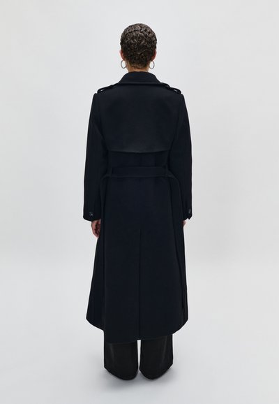 Lungo trench coat nero con un design doppiopetto, ampia collana, vita con cintura e polsini abbottonati. Tessuto liscio con una vestibilità su misura.