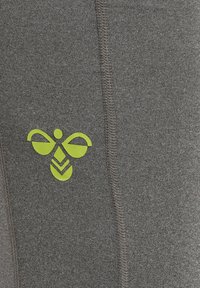 Zielone stylizowane logo pszczoły nadrukowane na szarej tkaninie z widocznym pionowym ściegiem.