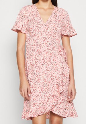 Frau trägt ein kurzärmeliges pinkes Wickelkleid mit kleinem Blumenmuster und Rüschen am Saum und an den Ärmeln.