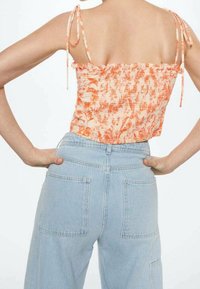 Top corto con motivo floreale in arancione e crema, con bordi arricciati e spalline legate, abbinato a jeans in denim azzurro chiaro a vita alta con tasche posteriori.