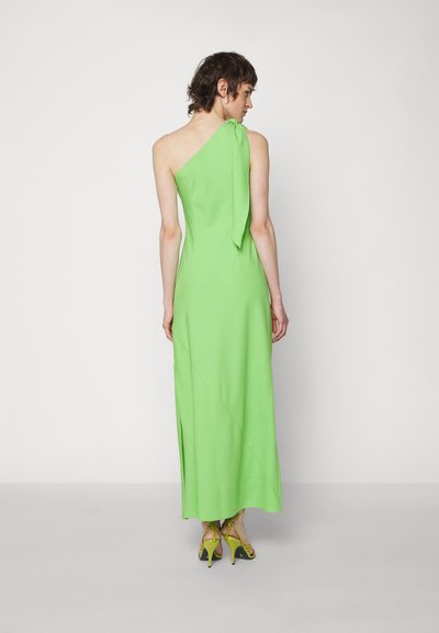 Πράσινο, μίντι φόρεμα με έναν ώμο και λεπτομέρεια δέσιμου, με απαλό υλικό και ψηλή σχισμή. Φοριέται με κίτρινες ψηλοτάκουνες σандάλες.