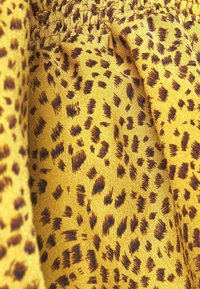 Gul tyg med ett strukturerat djurtryck i mörkbruna fläckar, som visar en slät, sidenaktig yta och detaljer med en sammetskrage.