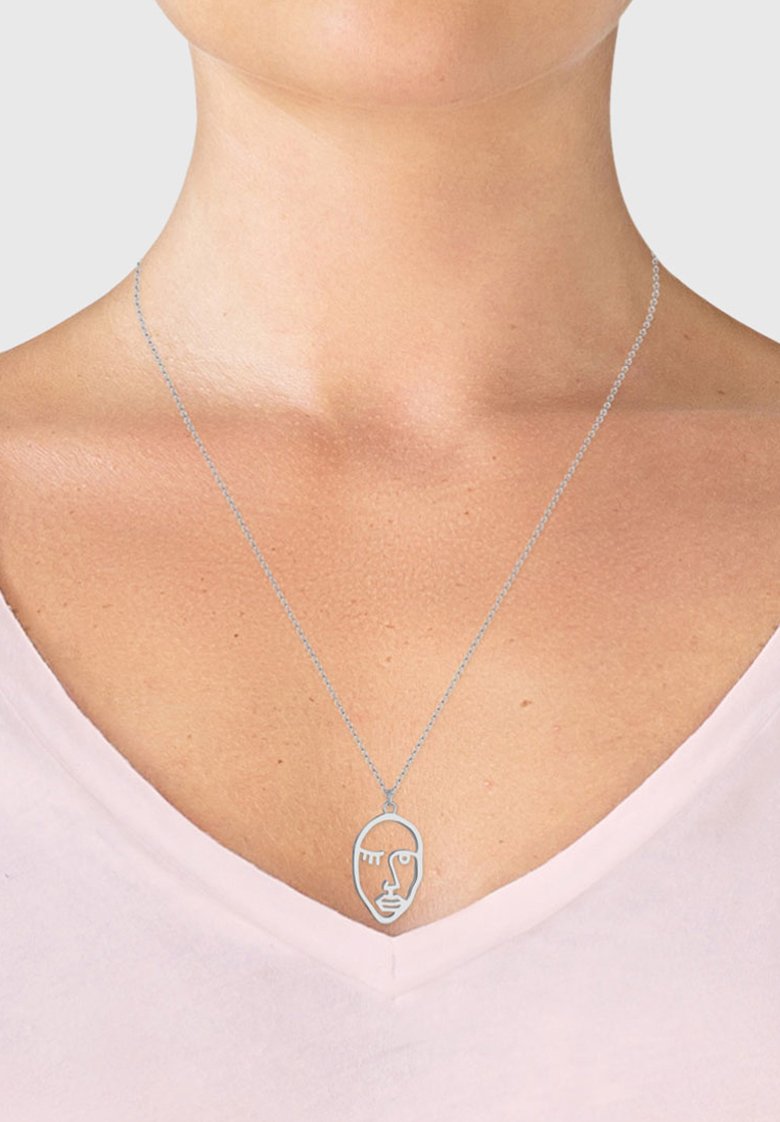 Silberne Halskette mit einem minimalistischen Gesichtdesign und einer stilisierten Handgeste, die an einer feinen Kette hängt und über einem hellrosa Oberteil getragen wird.