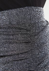 Tissu métallique argenté avec un design texturé et froncé, présentant une surface brillante et un éclat subtil, complété par une section noire.