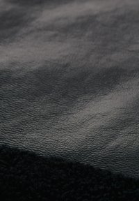 Schwarzes Leder und schwarzer Strukturstoff kombiniert, zeigen eine glatte, glänzende Oberfläche und eine weiche, pelzige Textur entlang der Kante.