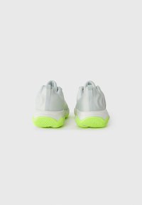 Baskets de sport gris clair avec une tige texturée, bout rond et semelles jaune-vert vif. Équipées de deux languettes pour un enfilage facile.