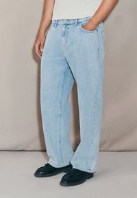 Light blue denim jeans with a relaxed fit, straight legs, front pockets, and a classic waistband. Worn with black shoes.