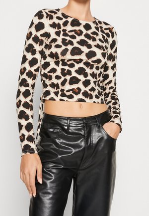 Afgekorte longsleeve met luipaardprint gecombineerd met hoog getailleerde zwarte leren broek, één hand in de zak, middel bloot.